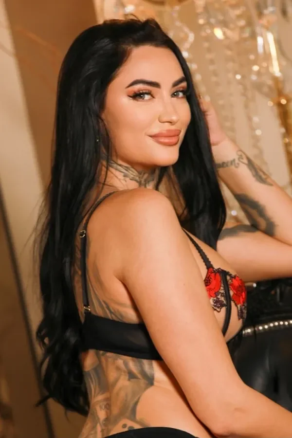 Foxy smiling over her shoulder in black and red floral lingerie beside a crystal chandelier